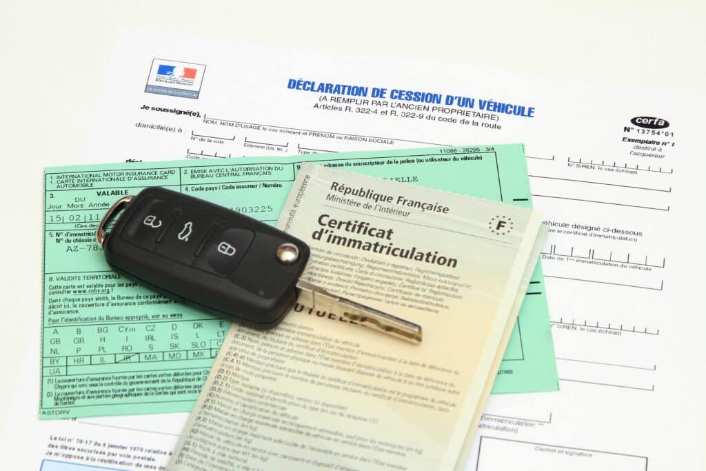 Documents administratifs français (déclaration de cession, certificat d'immatriculation, carte d'assurance auto verte) et une clé de voiture posés sur un fond blanc.